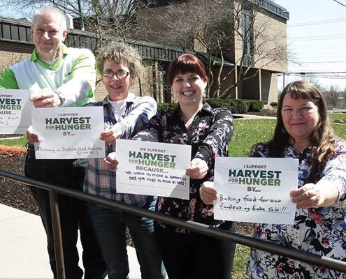 People smiling, holding up Harvest for Hunger signs.